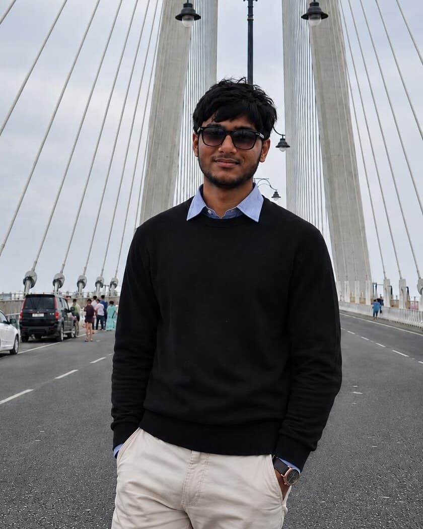 Ashish Dhankecha standing on a cable-stayed bridge, in a black sweater and sunglasses